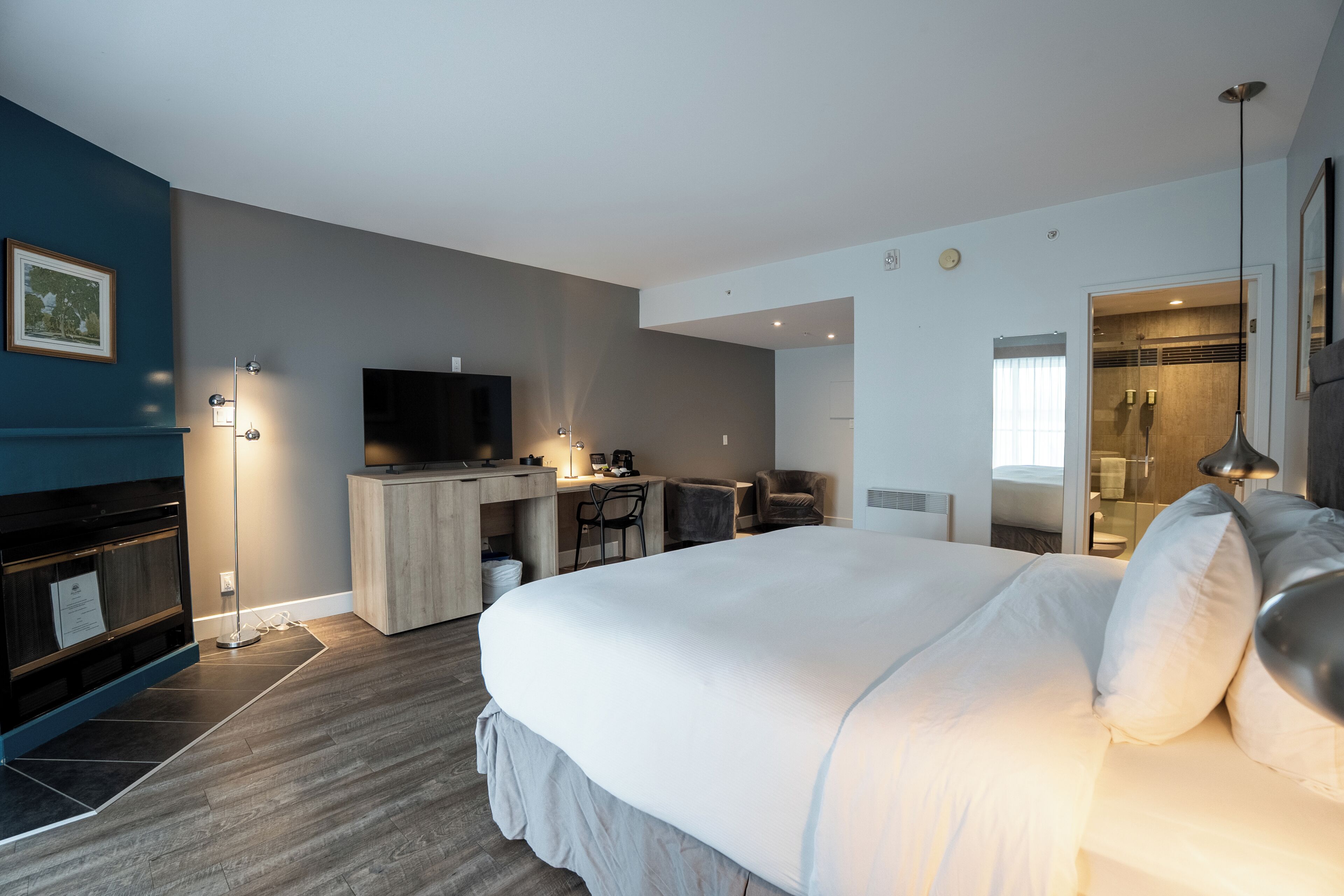 A modern hotel room with a large bed, a desk with a computer, a flat-screen TV, and a separate bathroom area.