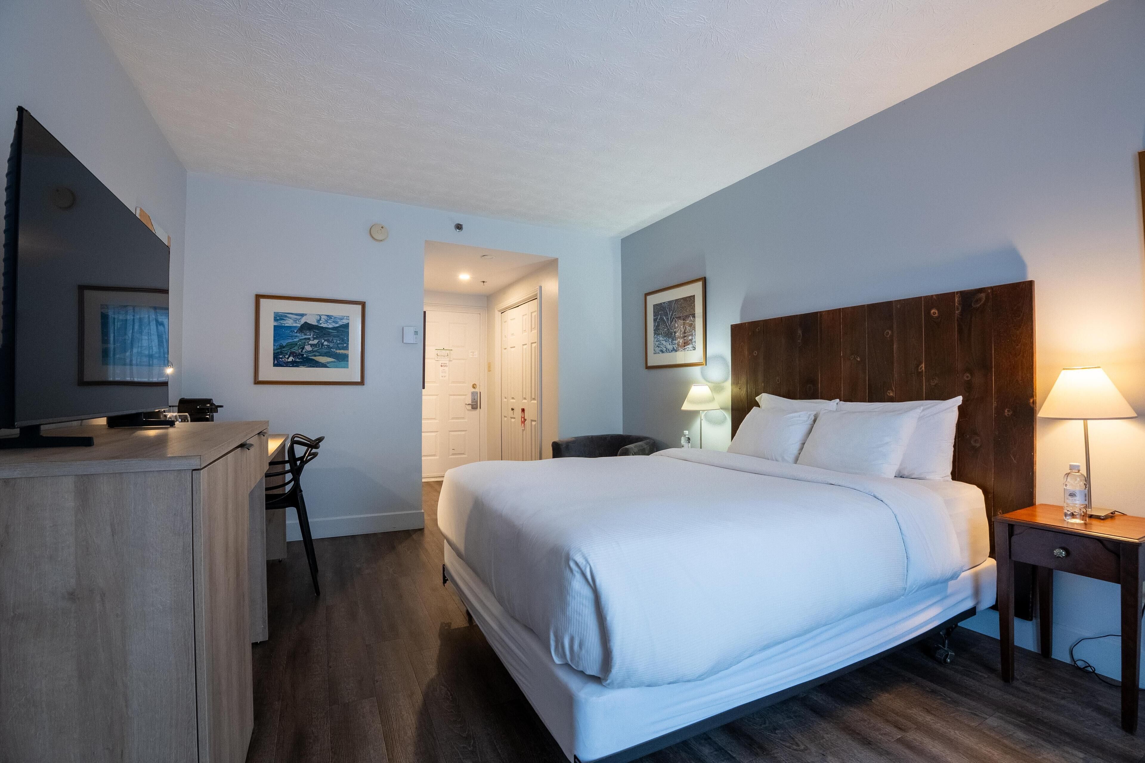 A hotel room with a bed, bedside table, lamp, and a desk with a chair.