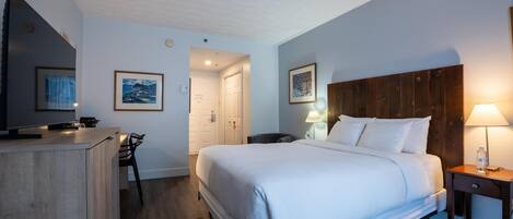 Habitación de hotel con cama, mesita de noche, lámpara y escritorio con silla.