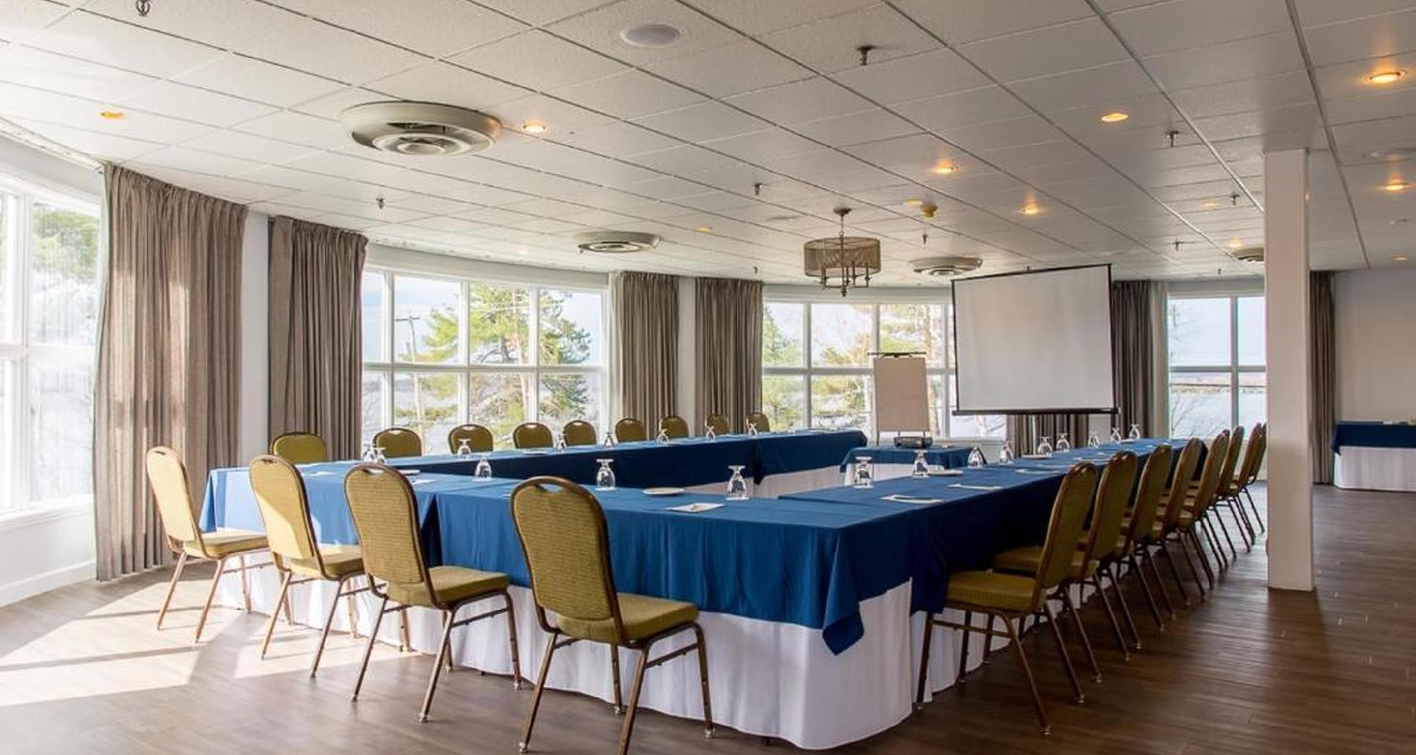 A conference room with a long table, chairs, a projector screen, and windows.