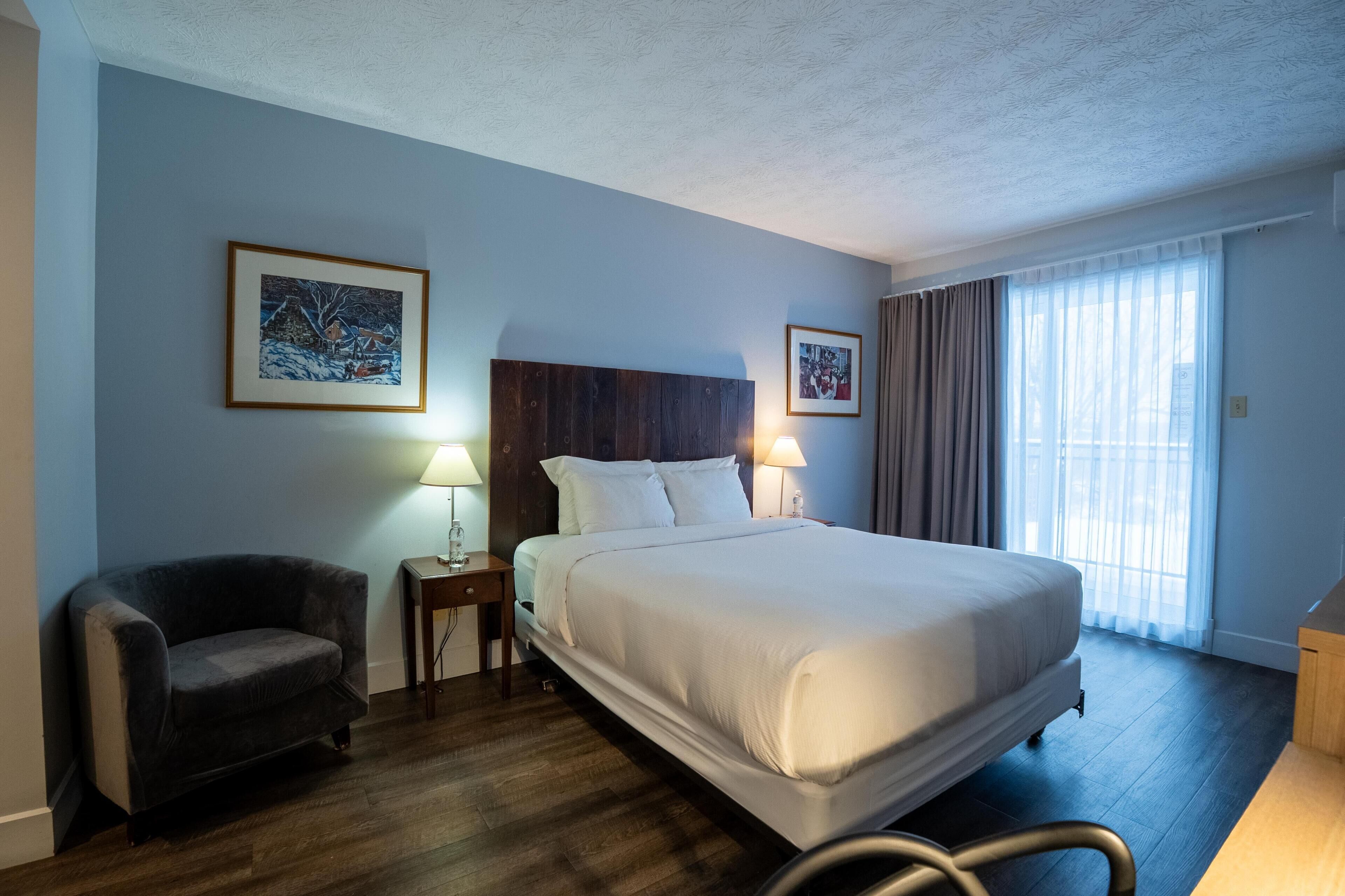 A hotel room with a large bed, a chair, a nightstand with a lamp, and two framed pictures on the walls.