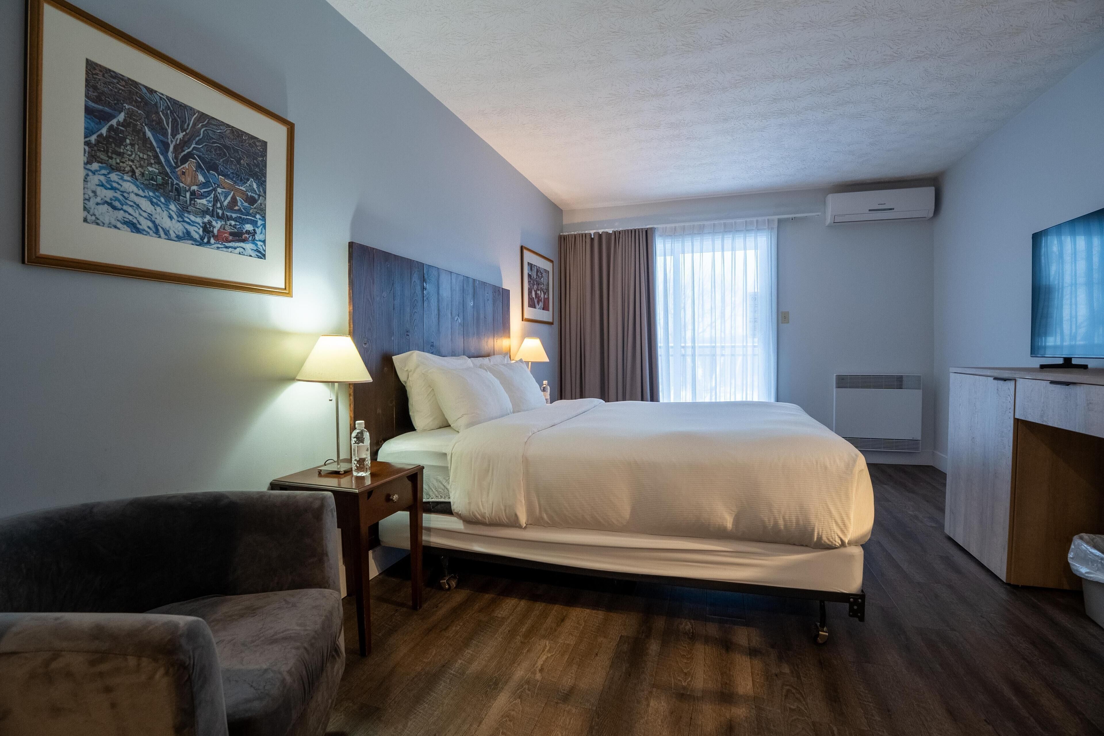 Una habitación de hotel con cama, mesitas de noche, una silla, un escritorio y televisión.