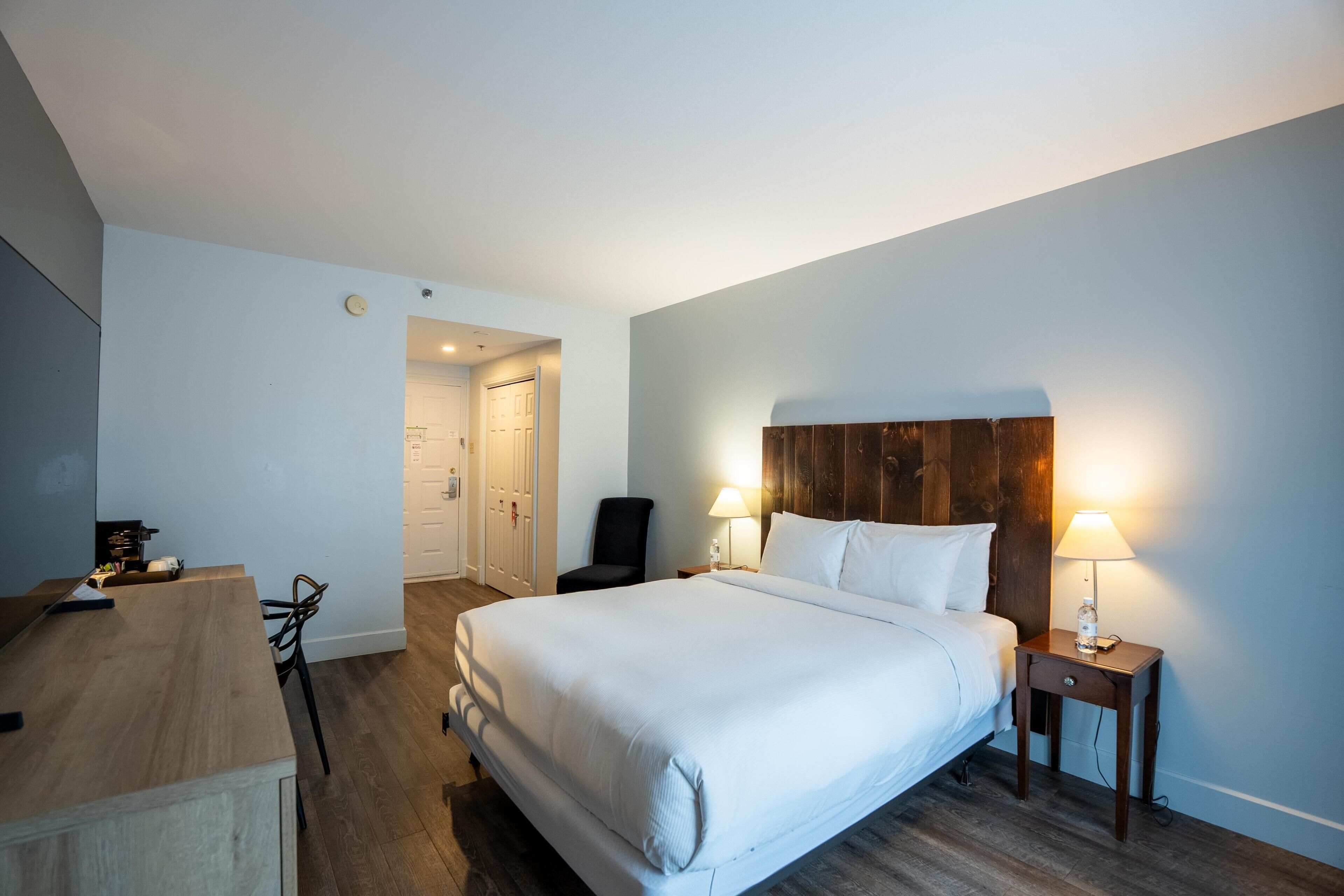 A hotel room with a bed, bedside tables, a chair, a desk, and a door leading to a bathroom.