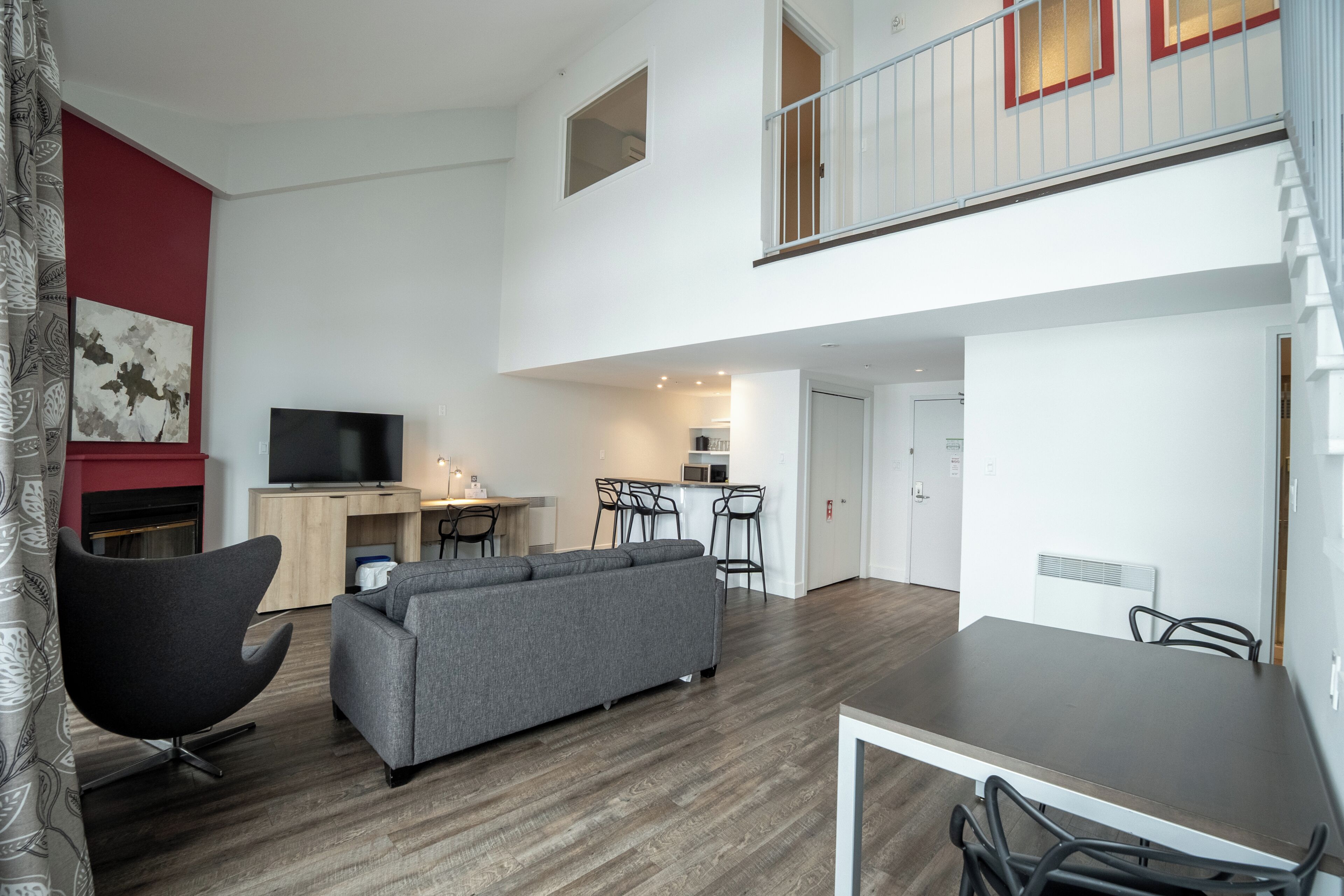 Een moderne woonkamer met een grijze bank, een flatscreen televisie en een eethoek met een tafel en stoelen.