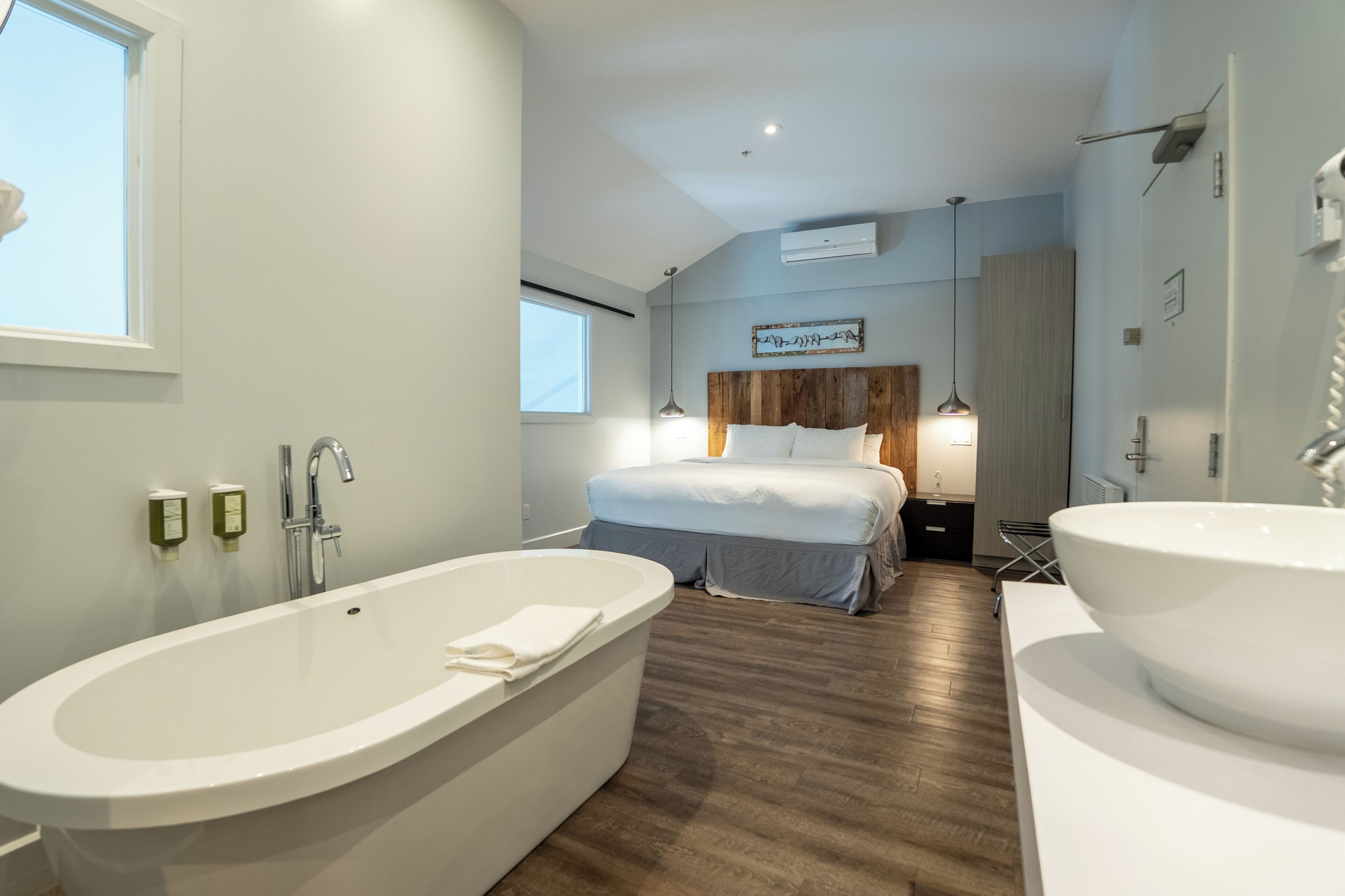 Una habitación de hotel moderna con una bañera grande, una cama doble y un baño separado con un lavamanos amplio.