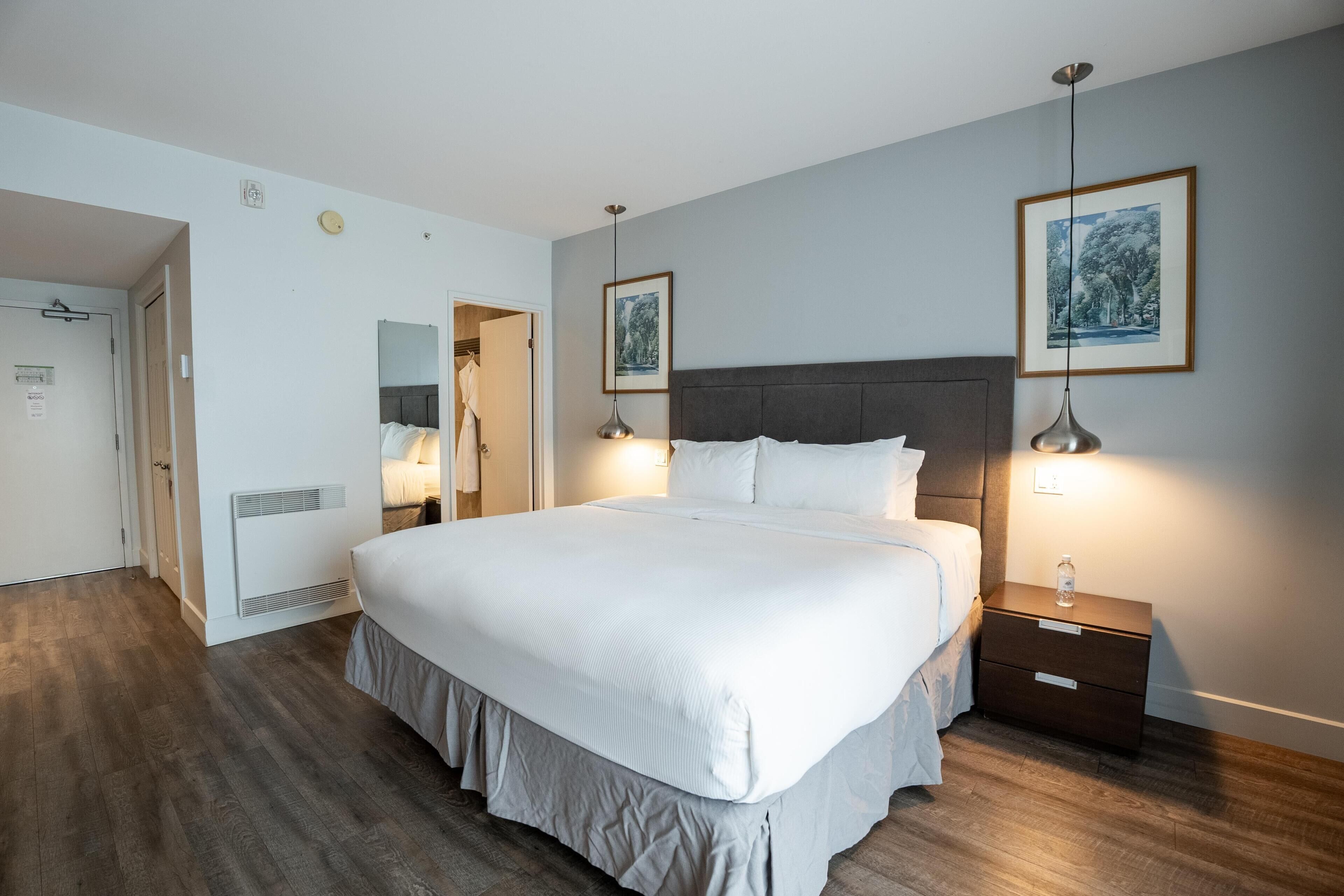 A hotel room with a large bed, bedside lamps, a nightstand, a mirror, and two framed pictures on the wall.