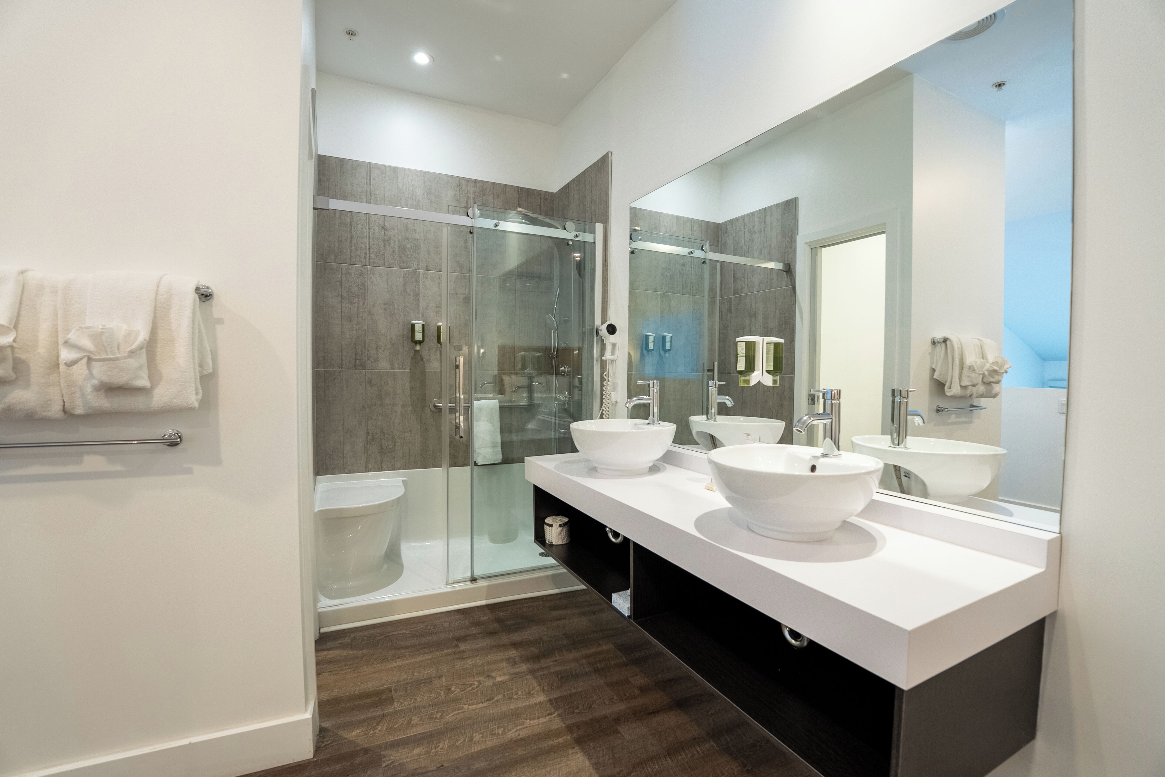 A modern bathroom with a glass shower enclosure, two sinks, and a large mirror.