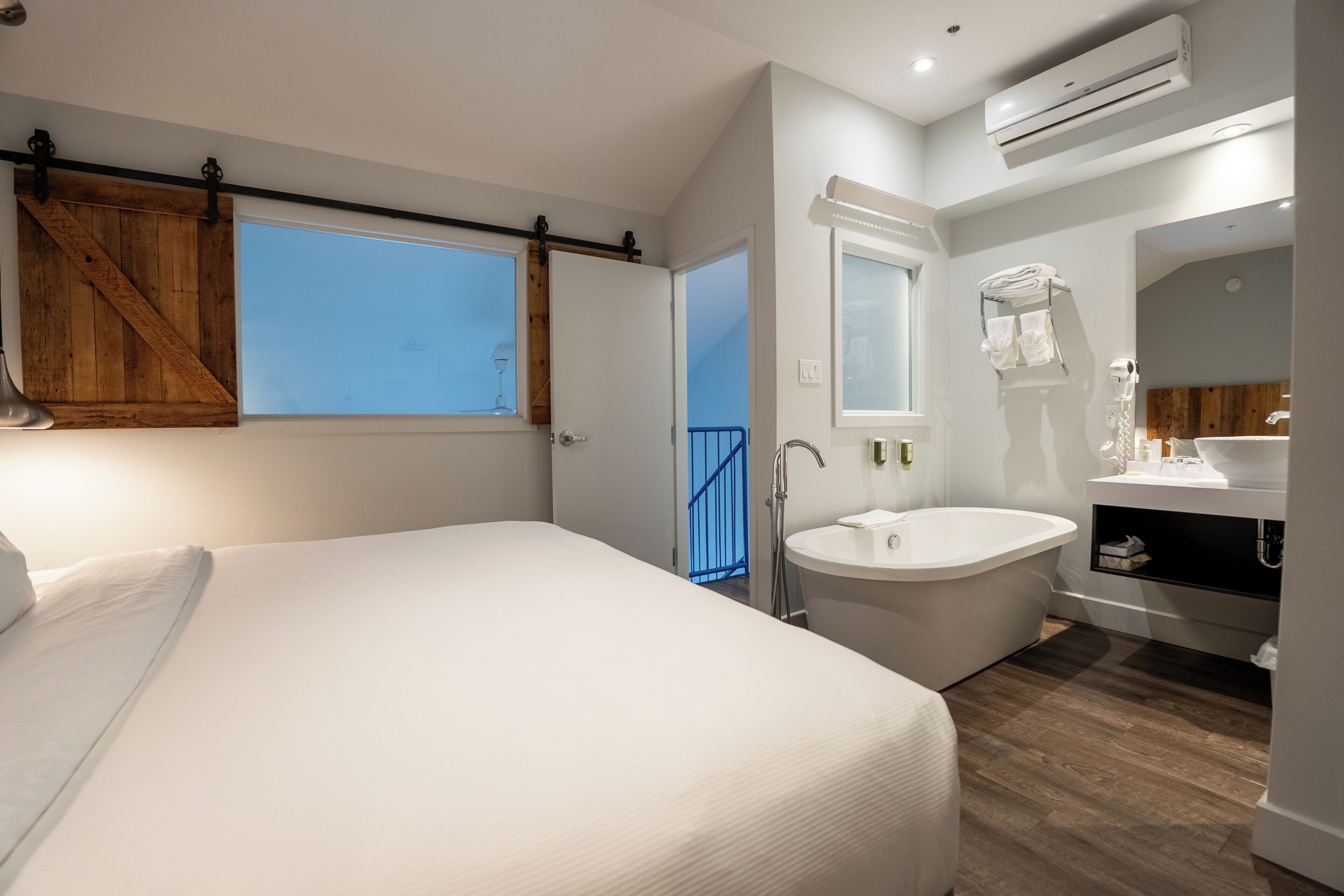 Quarto moderno com uma cama grande, banheiro com banheira e vista do céu pela janela.