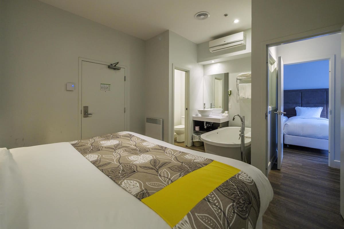 A hotel room with a bed, a bathroom with a sink and mirror, and an air conditioning unit on the wall.