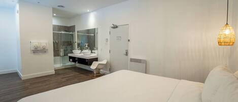 A modern bedroom with a large bed, a bedside table, a mirror, a shower area, and a hanging light fixture.