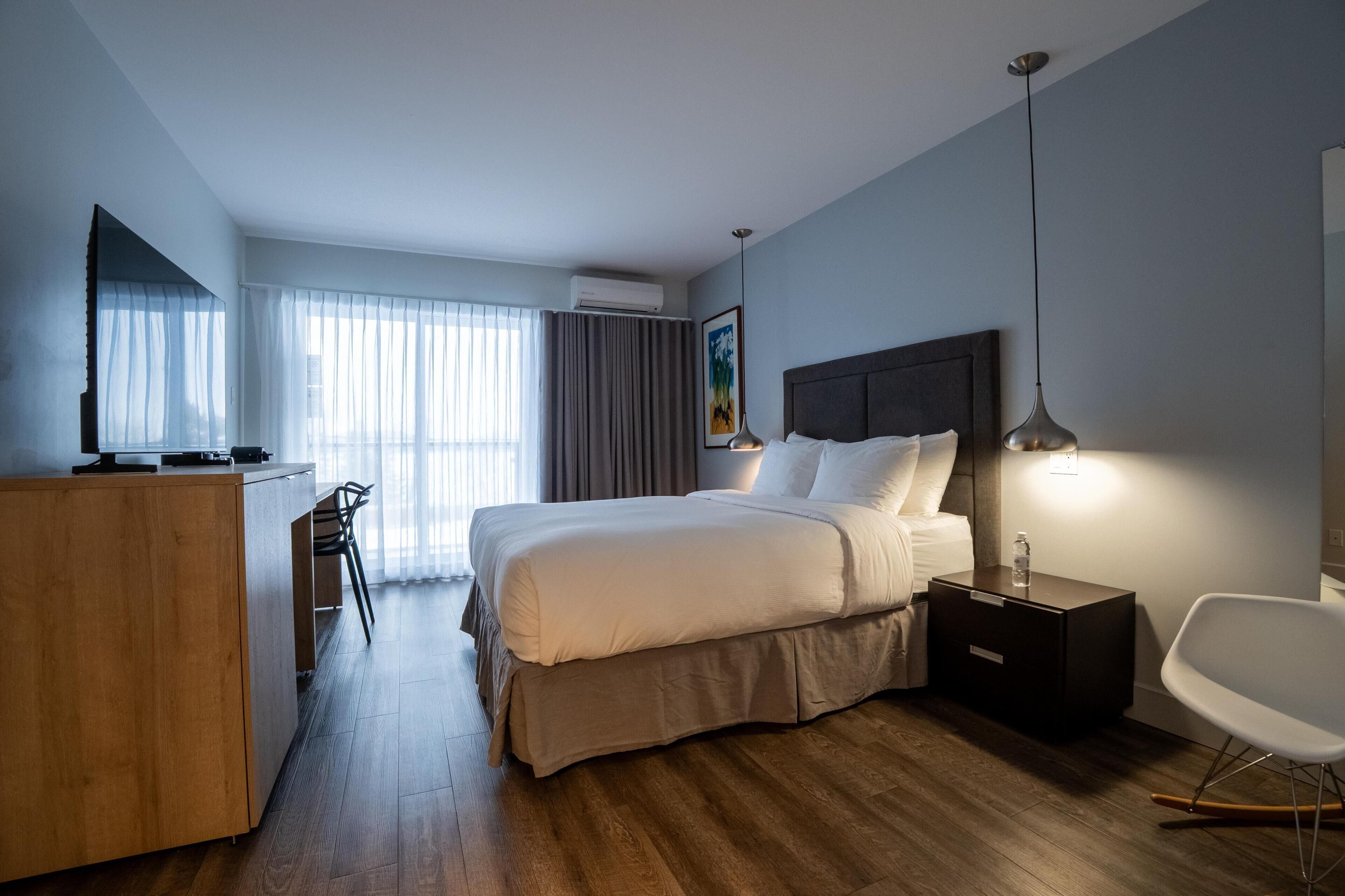 Habitación de hotel con cama, escritorio, silla, televisor y un cuadro en la pared.