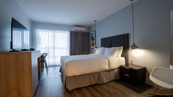 Habitación de hotel con cama, escritorio, silla, televisor y un cuadro en la pared.