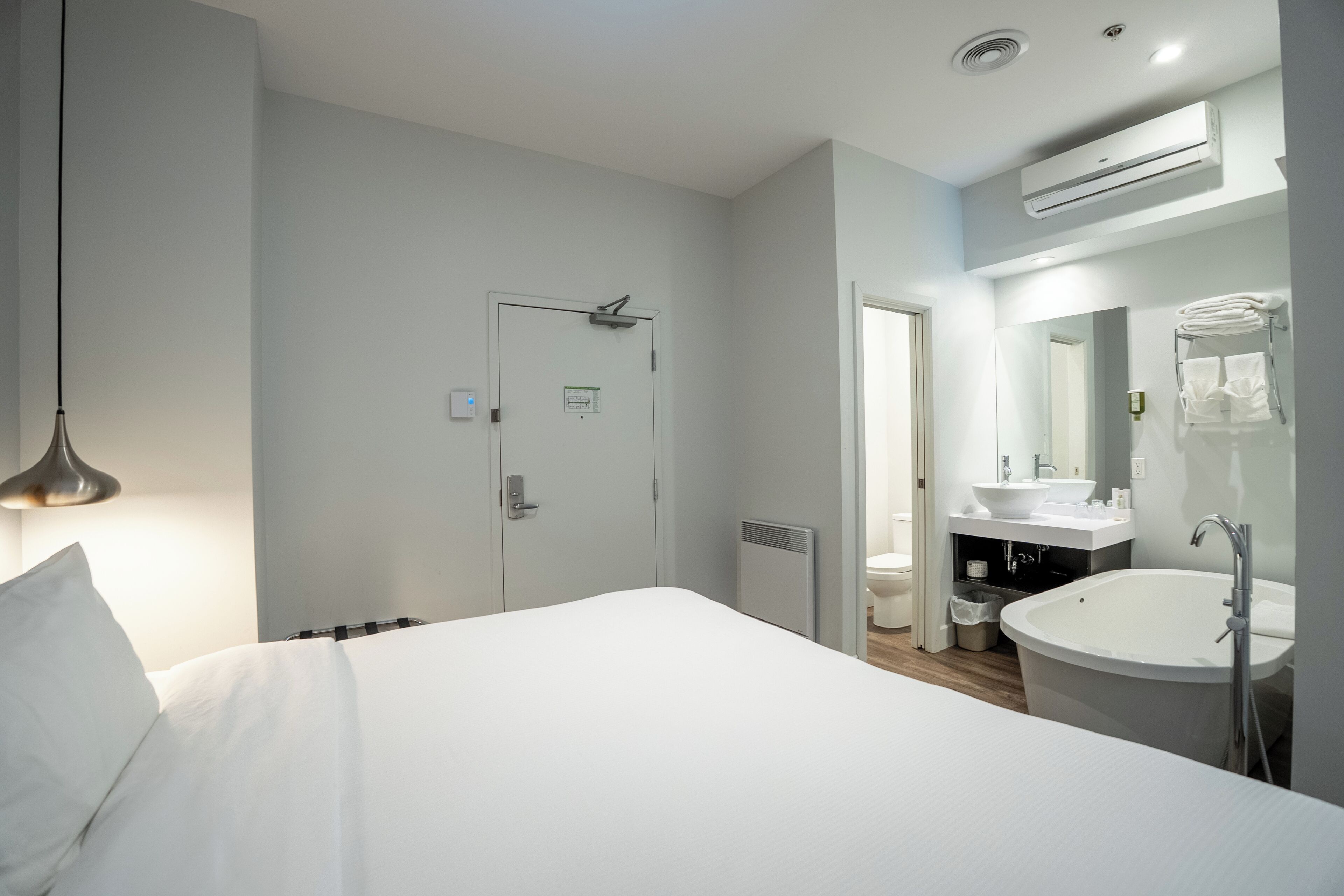 A hotel room with a bed, a large mirror, a sink, and an air conditioning unit.