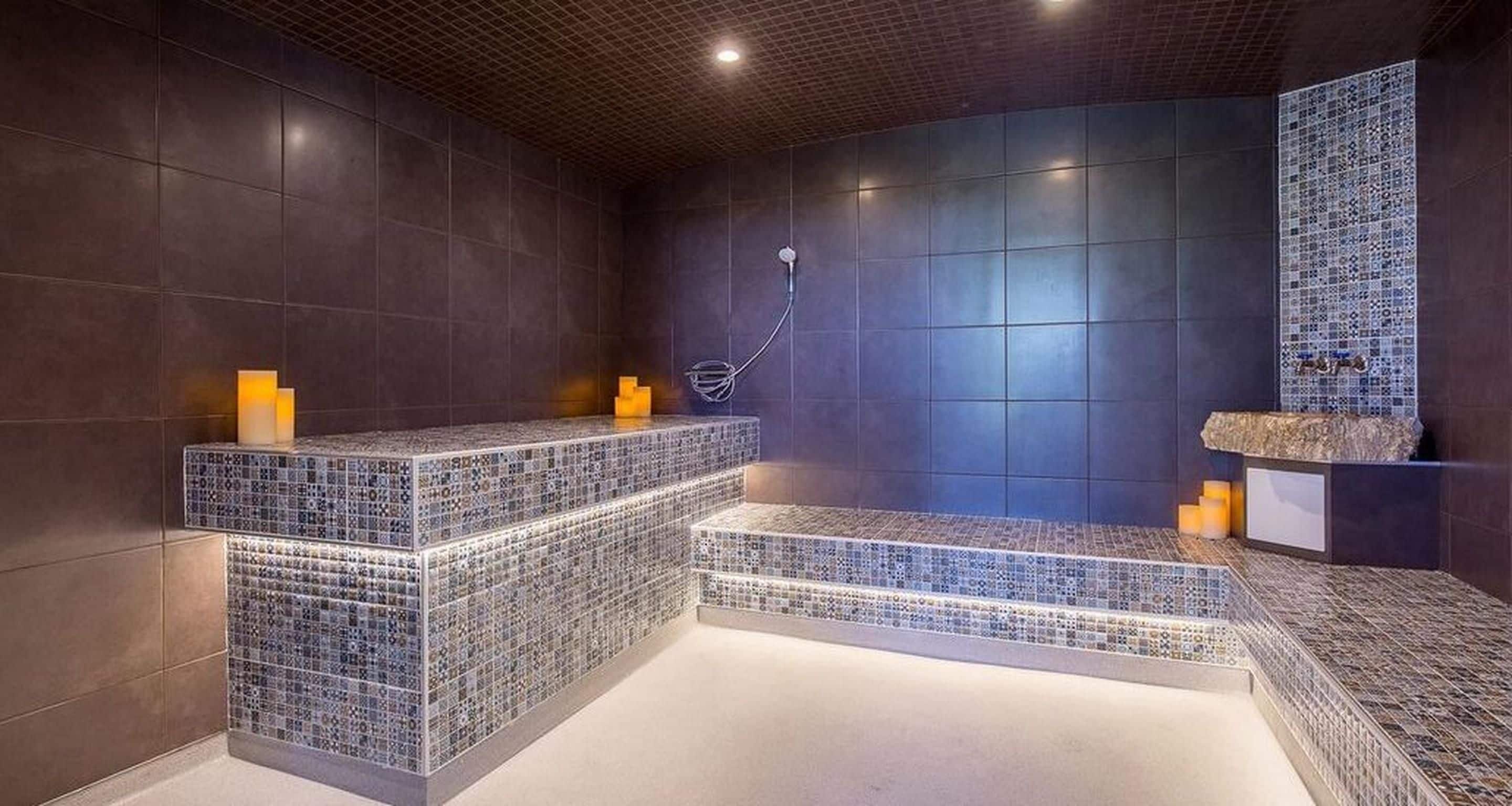 A modern bathroom with a dark tiled wall, a built-in bench, and a shower area.