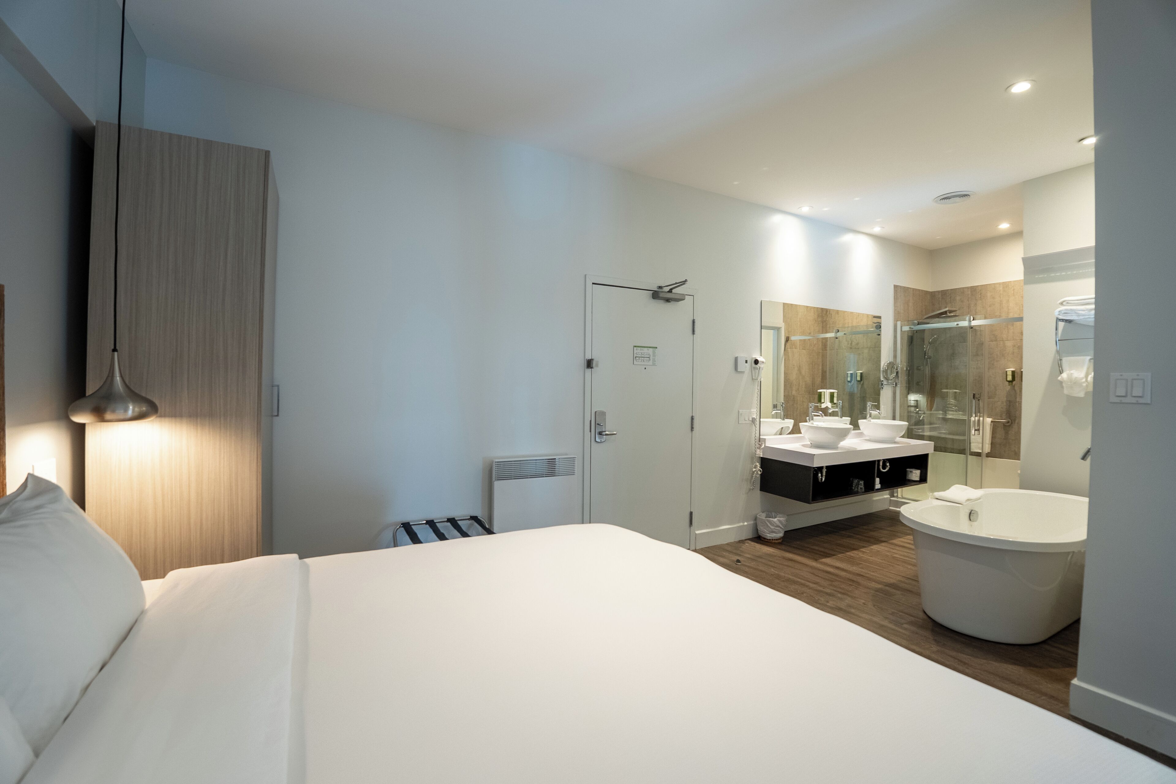 Une chambre d’hôtel moderne dotée d’un grand lit, d’une salle de bain avec douche et d’un meuble-lavabo avec deux vasques.