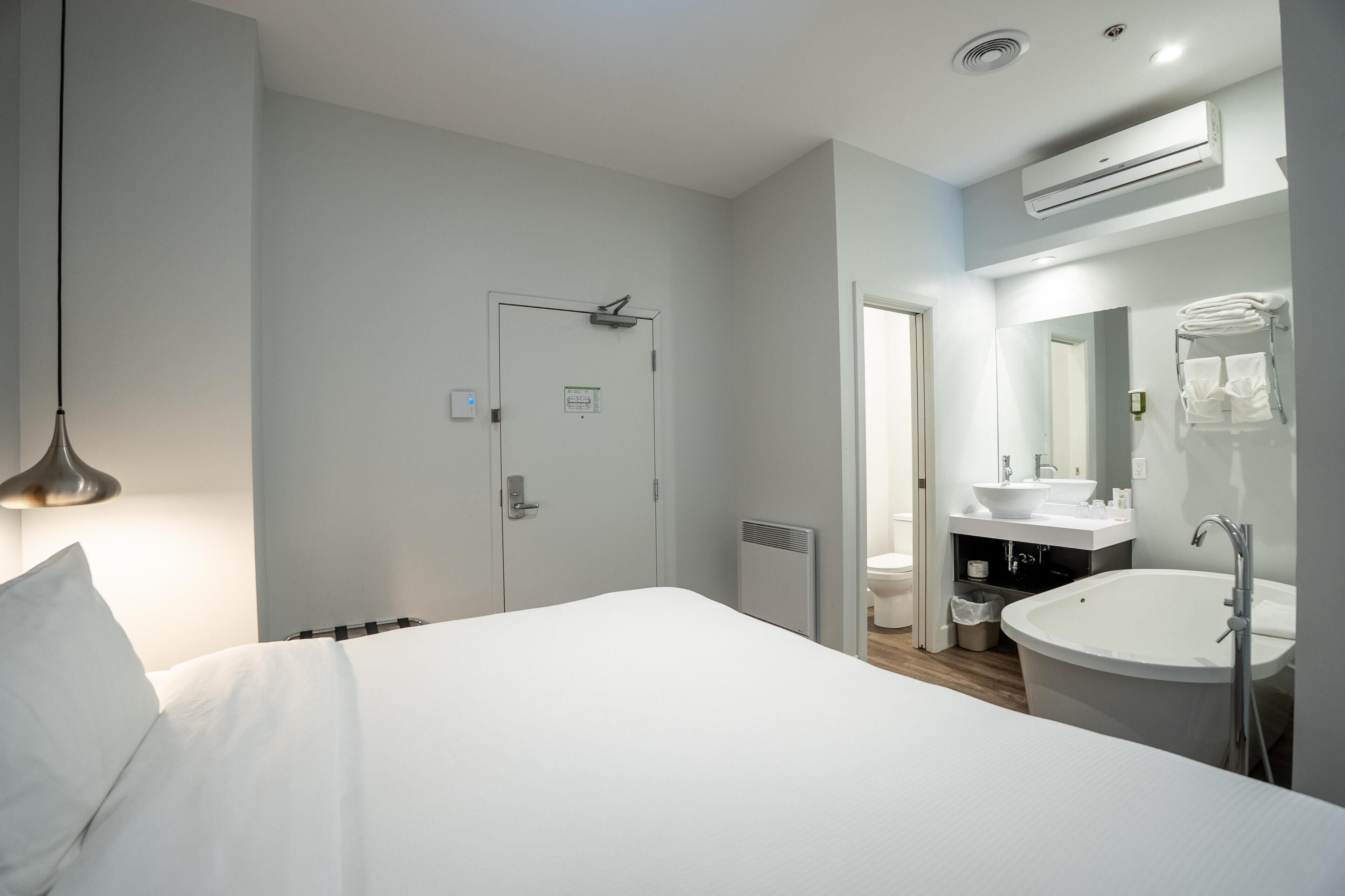 Ein Hotelzimmer mit einem Bett, einem Badezimmer mit Waschbecken und Spiegel sowie einer Klimaanlage.