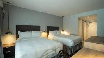 Habitación de hotel con dos camas, un escritorio y un baño visible a través de una puerta abierta.