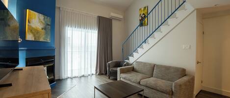 A living room with a sofa, a coffee table, a staircase with blue railings, and a painting on the wall.