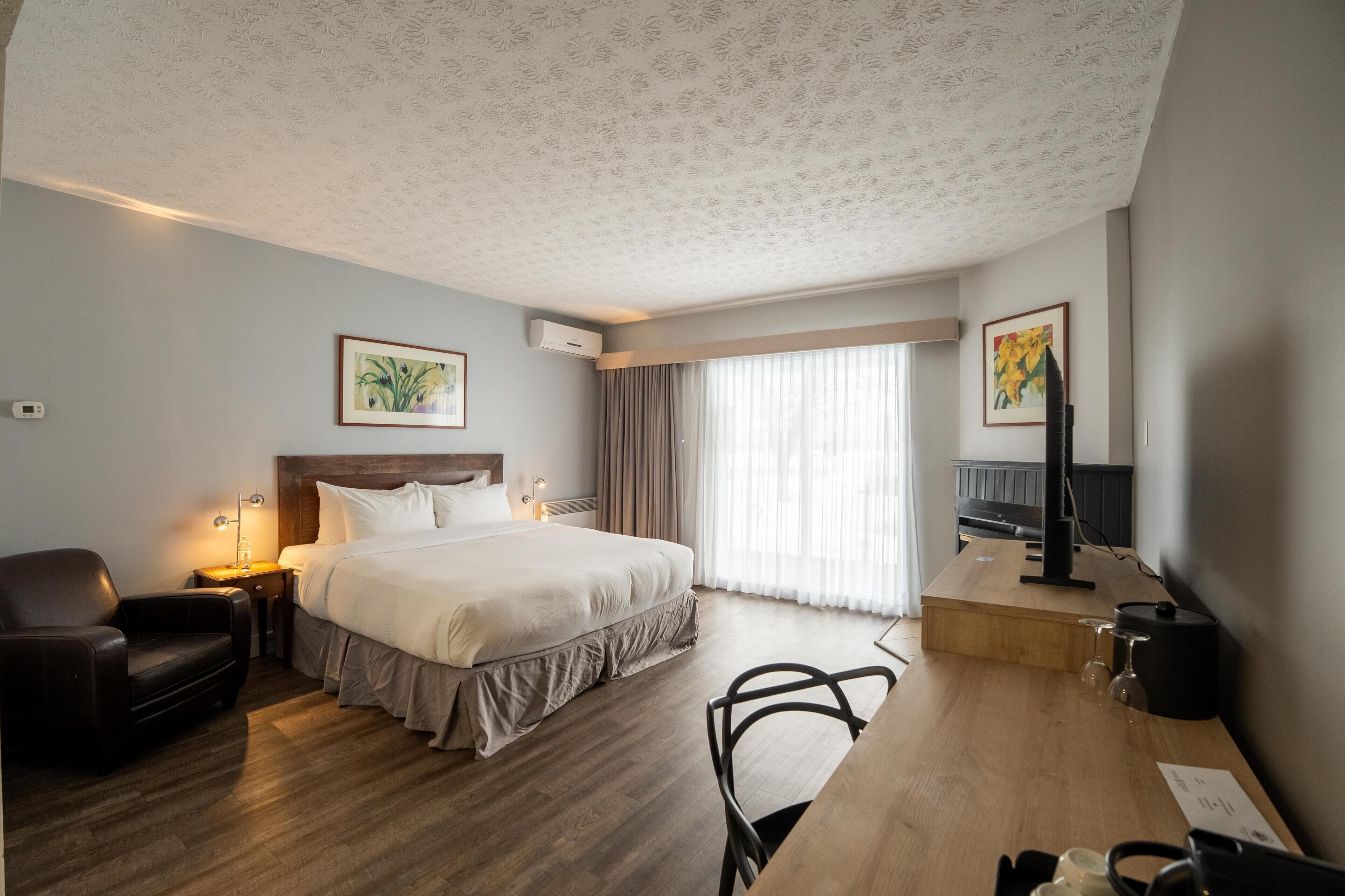 Habitación de hotel con cama, escritorio, silla, televisor y ventana con cortinas.