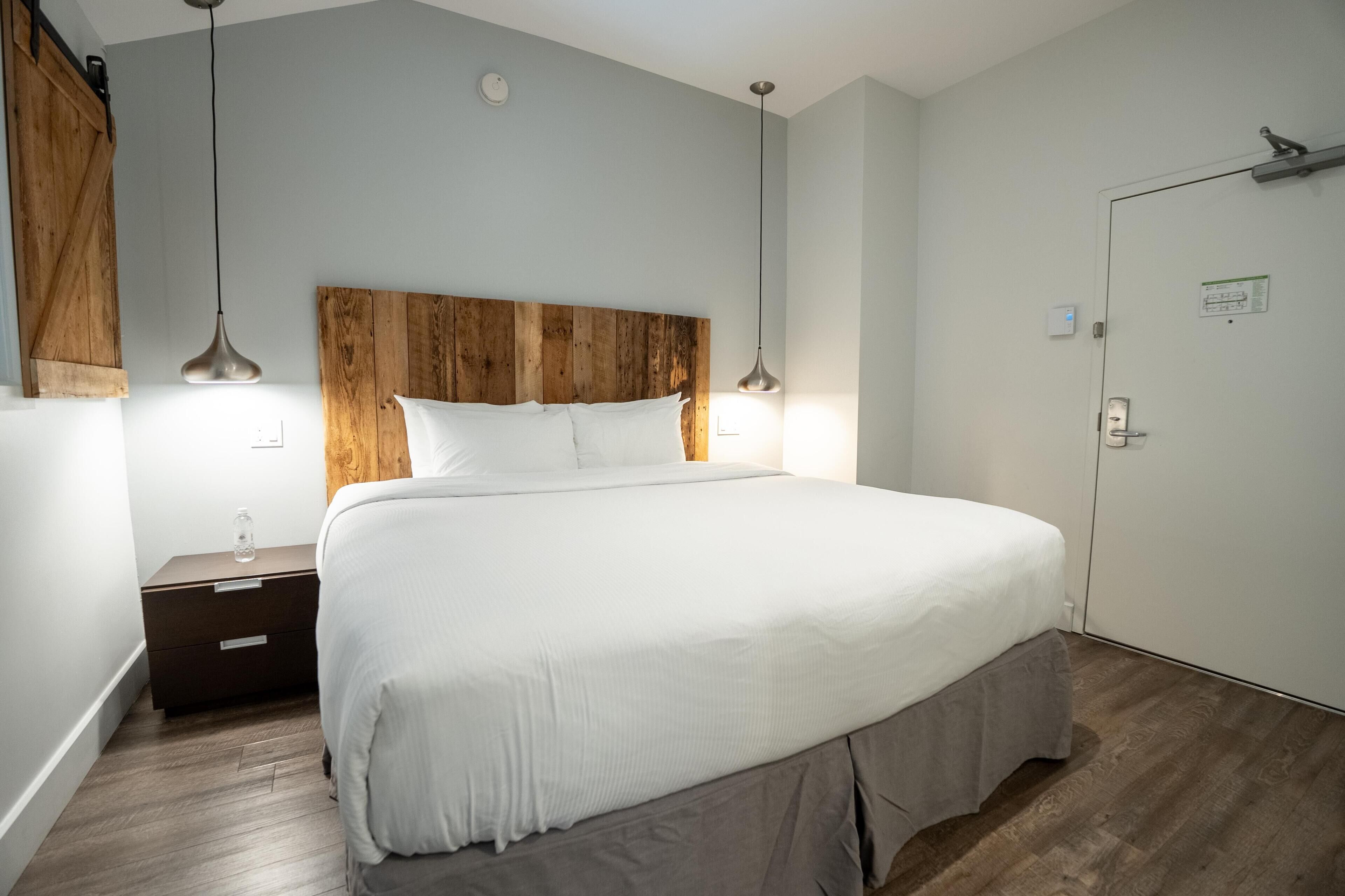 A bedroom with a large bed, wooden headboard, bedside tables, and pendant lights.