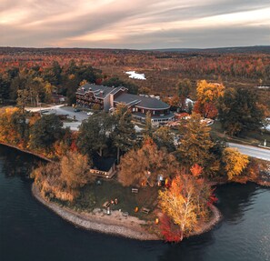A large, multi-story building with a circular central section, surrounded by trees and a body of water. - Hotel Lac Brome, BW Signature Collection (Lac-Brome)