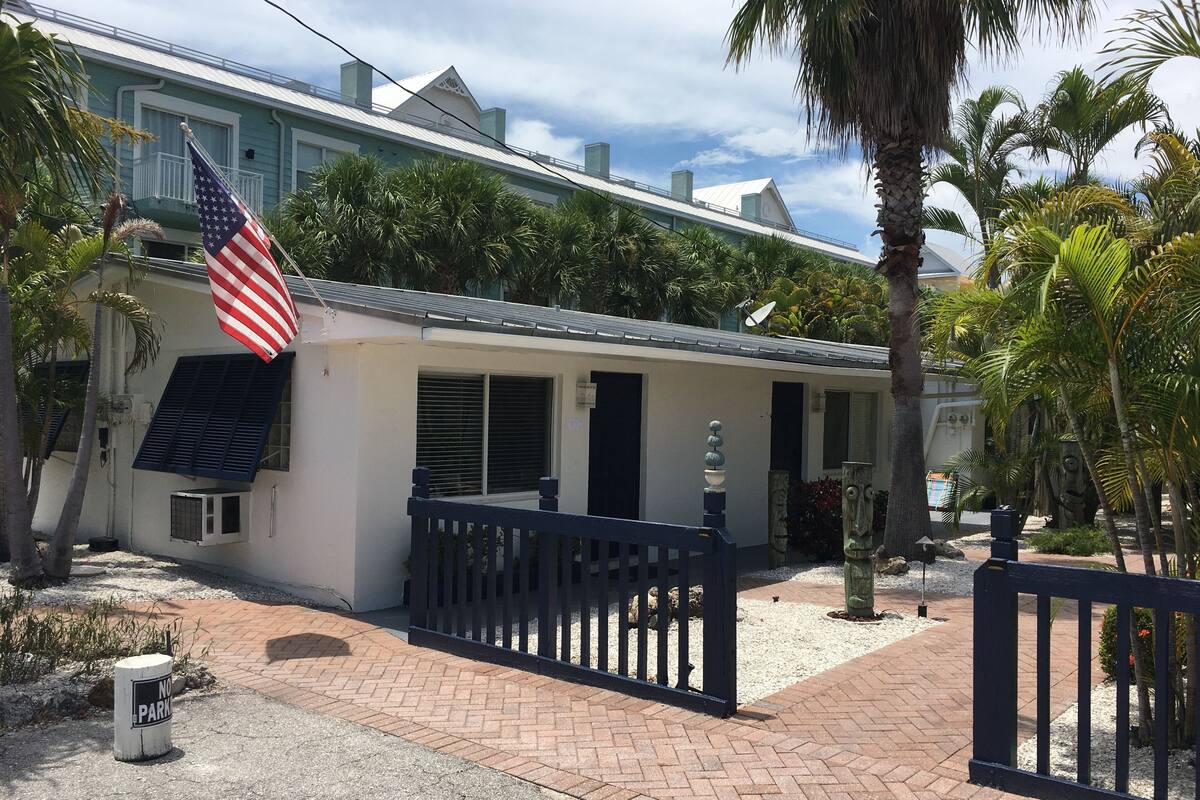 Ein zweistöckiges Haus mit weißer Fassade, einem Balkon mit schwarzer Geländer und einer US-amerikanischen Flagge.