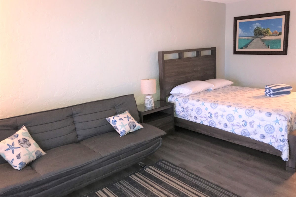 Ein Schlafzimmer mit Bett, Sofa, Nachttisch, Lampe und einem gerahmten Bild an der Wand.