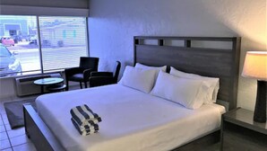 A hotel room with a large bed, a bedside table with a lamp, a chair, and a small table. - Bonita Beach Inn and Suites (Bonita Springs)
