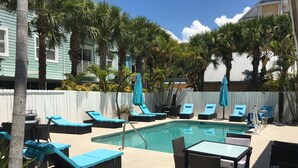 A pool area with lounge chairs and a table, surrounded by a white fence and palm trees. - Bonita Beach Inn and Suites (Bonita Springs)