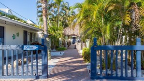 A pathway leading to a building with an 'Office' sign, surrounded by palm trees and a thatched-roof structure. - Bonita Beach Inn and Suites (Bonita Springs)