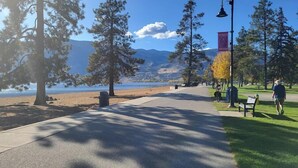 A park with a paved walkway, benches, and trees. - Travelers Motel (Penticton)