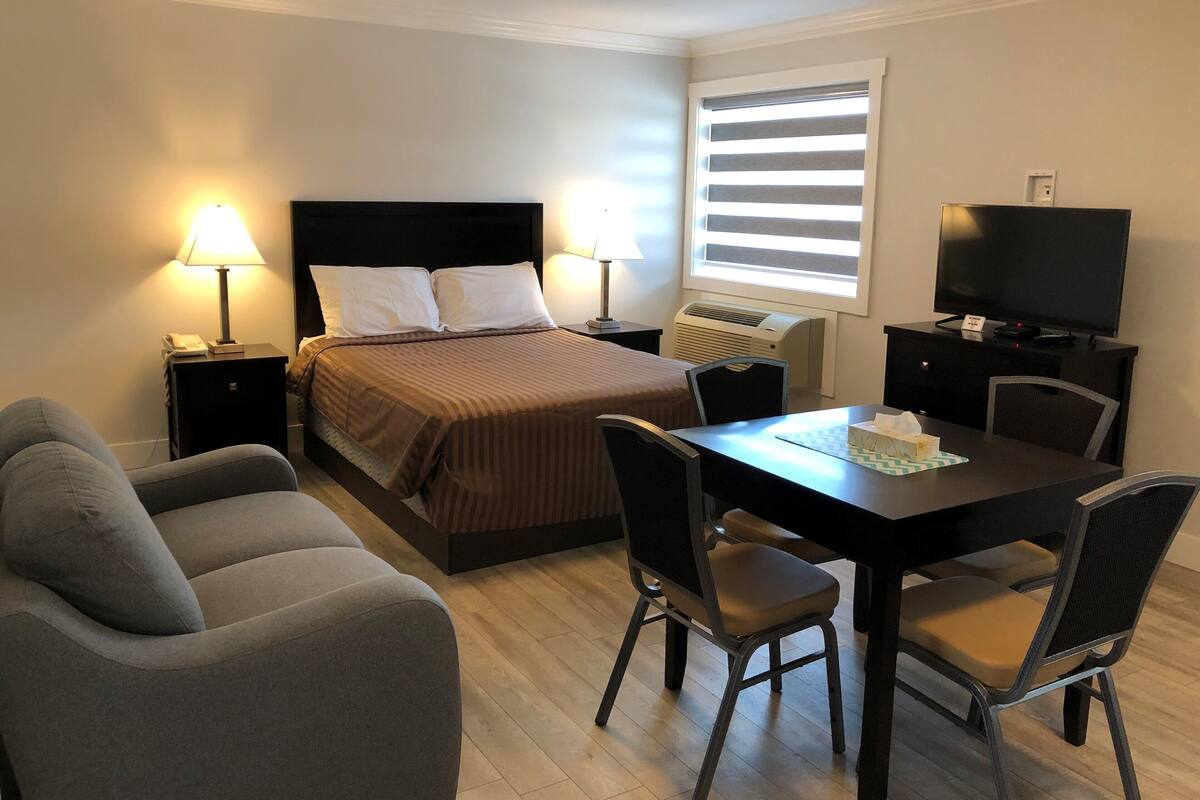 A hotel room with a bed, bedside lamps, a desk with a chair, a television, and a window with blinds.