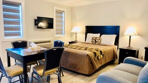 A hotel room with a bed, two bedside lamps, a desk with a chair, and a television on the wall. - Travelers Motel (Penticton)