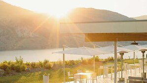 An outdoor seating area with tables and umbrellas, overlooking a body of water and hills. - Travelers Motel (Penticton)