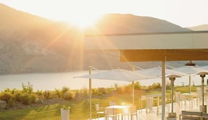 An outdoor seating area with tables and umbrellas, overlooking a body of water and hills.