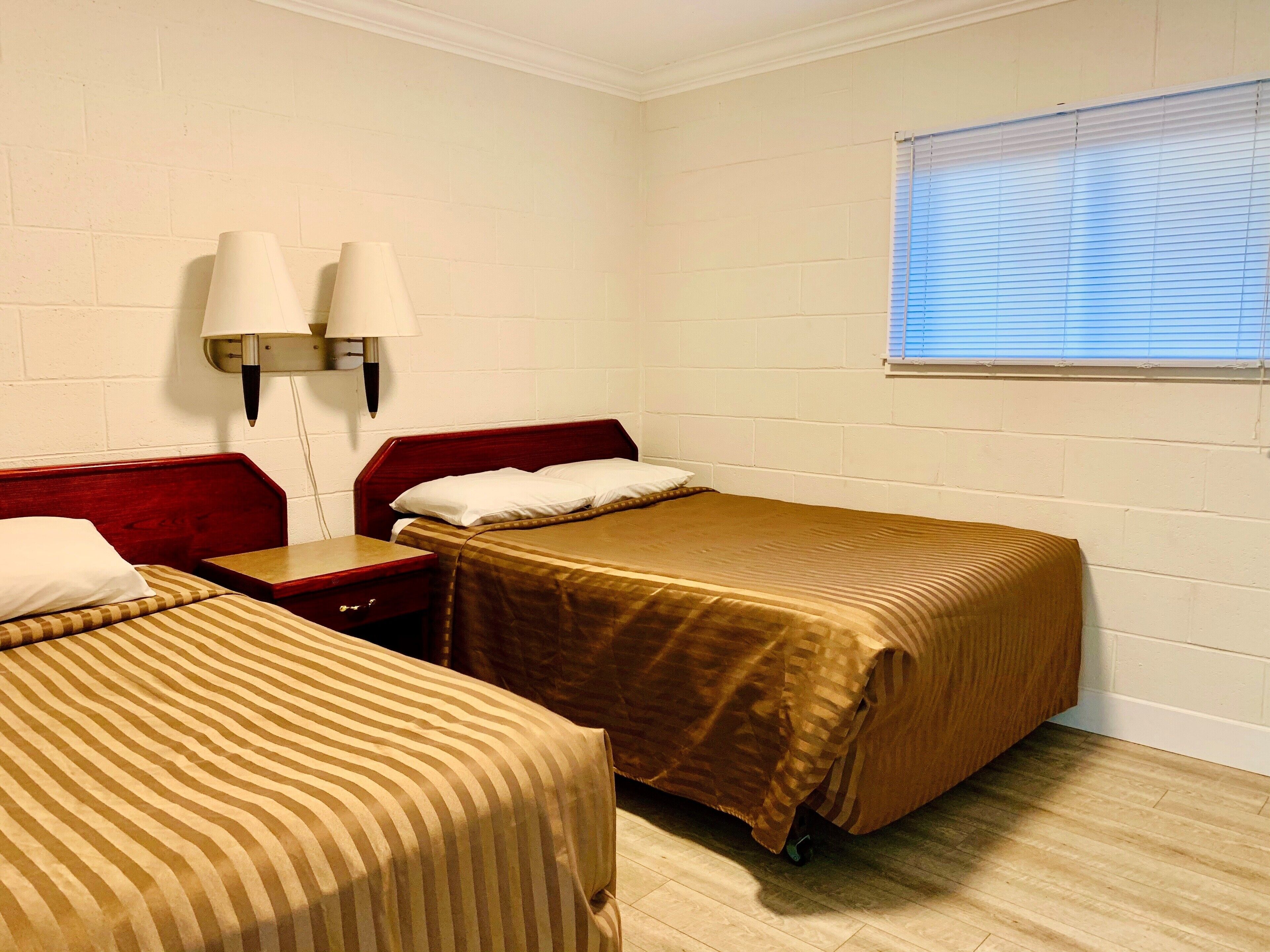 Habitación de hotel con dos camas individuales, una mesita de noche, una lámpara y una ventana con persianas.