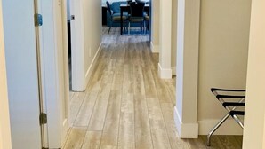 A hallway with wooden flooring, white walls, and a ceiling light. There is a dining area with a table and chairs visible in the distance. - Travelers Motel (Penticton)