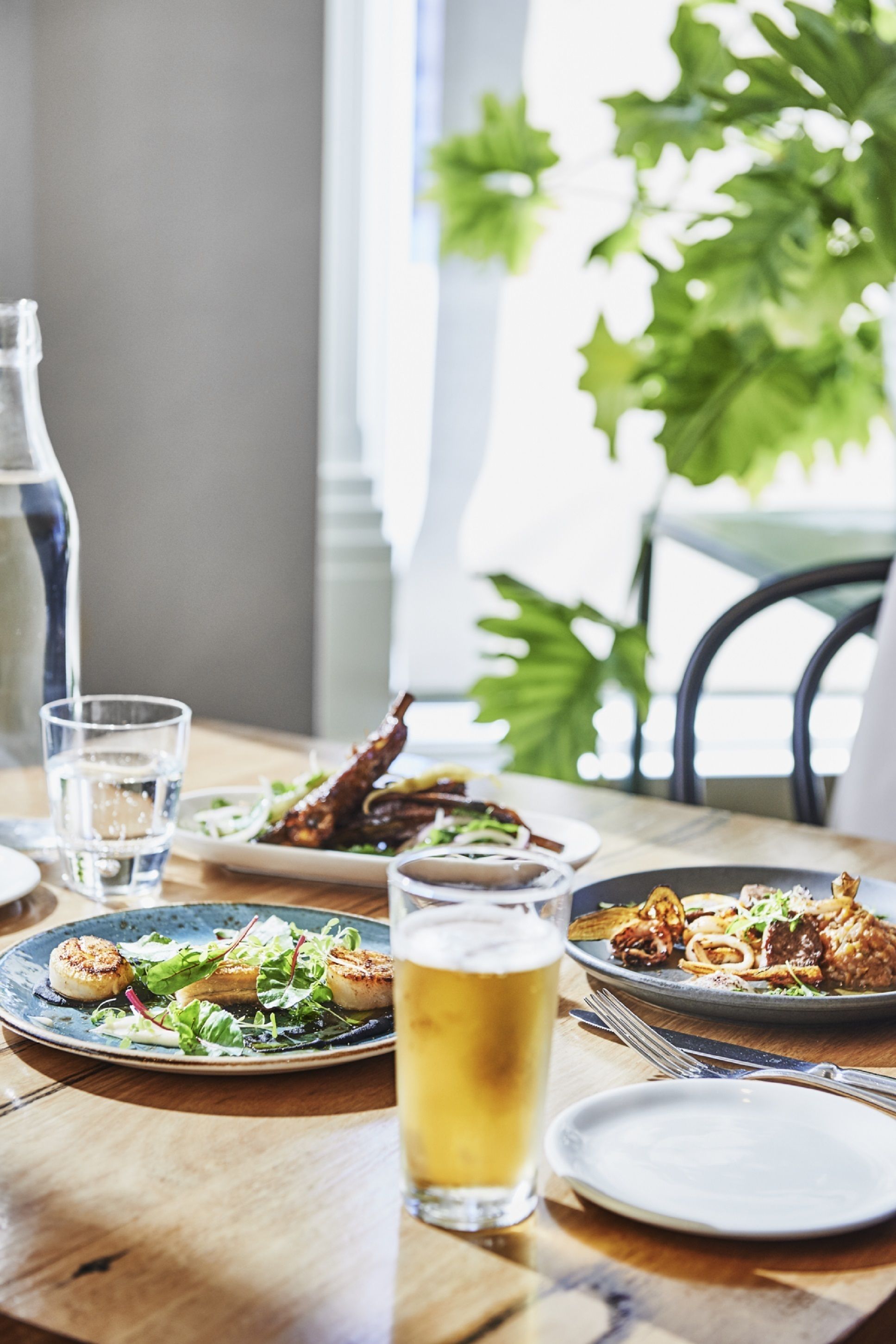 A dining table with plates of food, a glass of beer, and a water bottle.