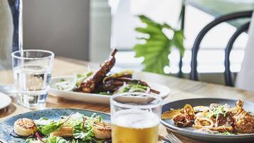 A dining table with plates of food, a glass of beer, and a water bottle.