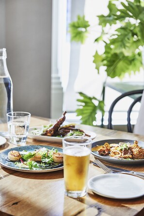 A dining table with plates of food, a glass of beer, and a water bottle. - Plough Hotel (Footscray)