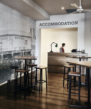 A bar area with stools and a counter, a wall mural of a building, and a sign reading "ACCOMMODATION". - Plough Hotel (Footscray)