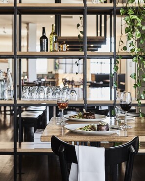 A dining table set with plates of food and wine glasses, surrounded by chairs. - Plough Hotel (Footscray)
