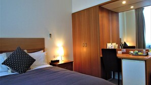 Ein Hotelzimmer mit Bett, Schreibtisch, Spiegel und kleinem Kühlschrank.