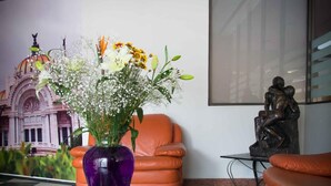 A lobby with a checkered floor, a purple vase with flowers, orange leather chairs, and a statue on a table. - Hotel Max (Mexico City)