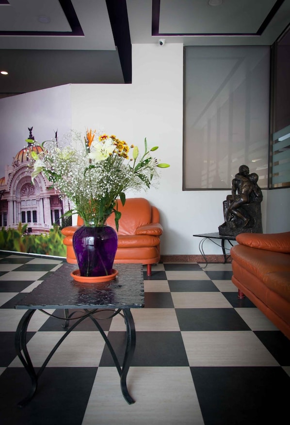 A lobby with a checkered floor, a purple vase with flowers, orange leather chairs, and a statue on a table.