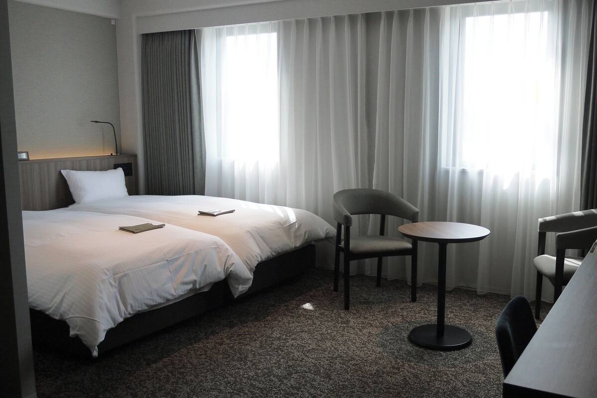 A hotel room with two beds, a small round table, two chairs, and a desk with a chair.