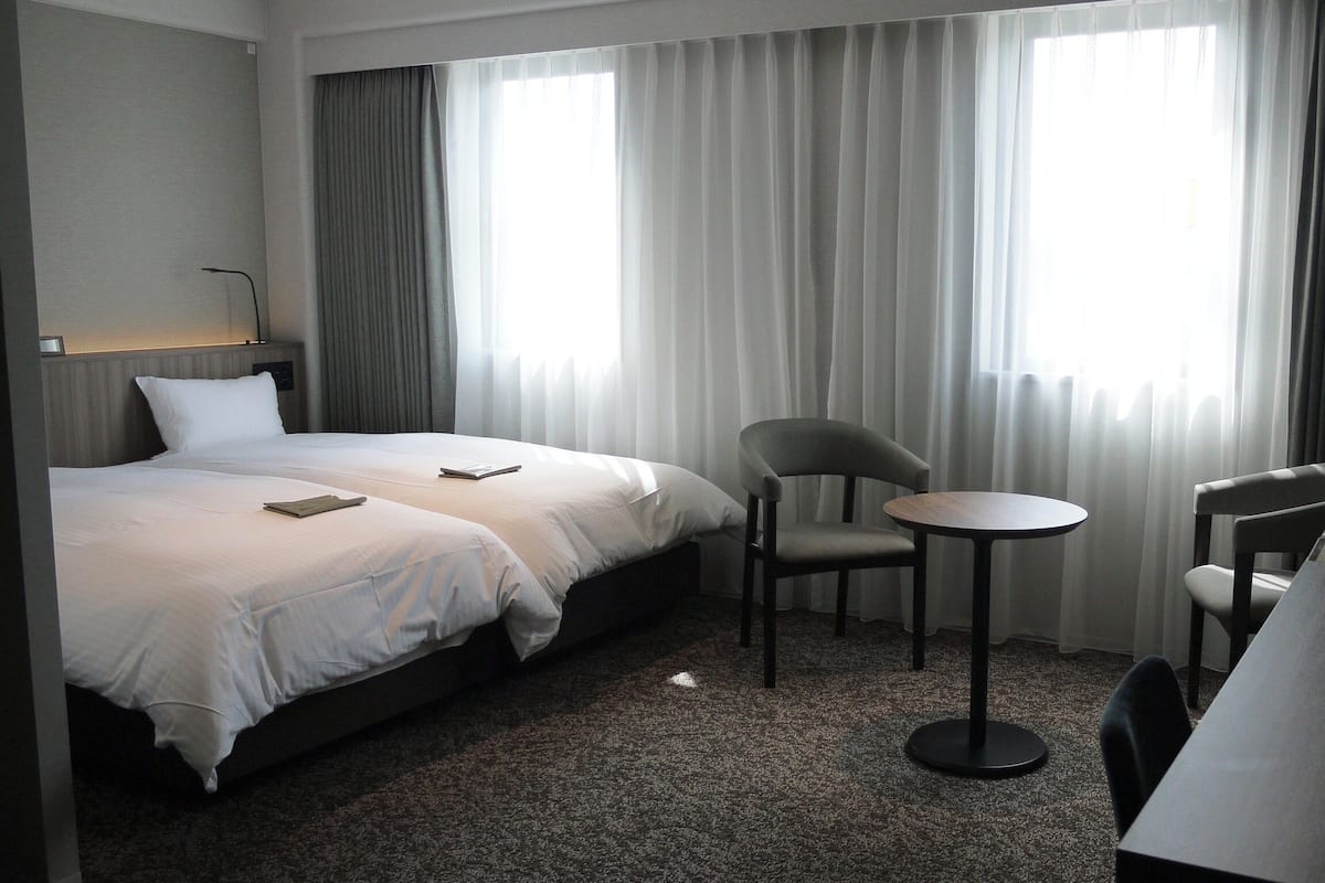A hotel room with two beds, a small round table, two chairs, and a desk with a chair.