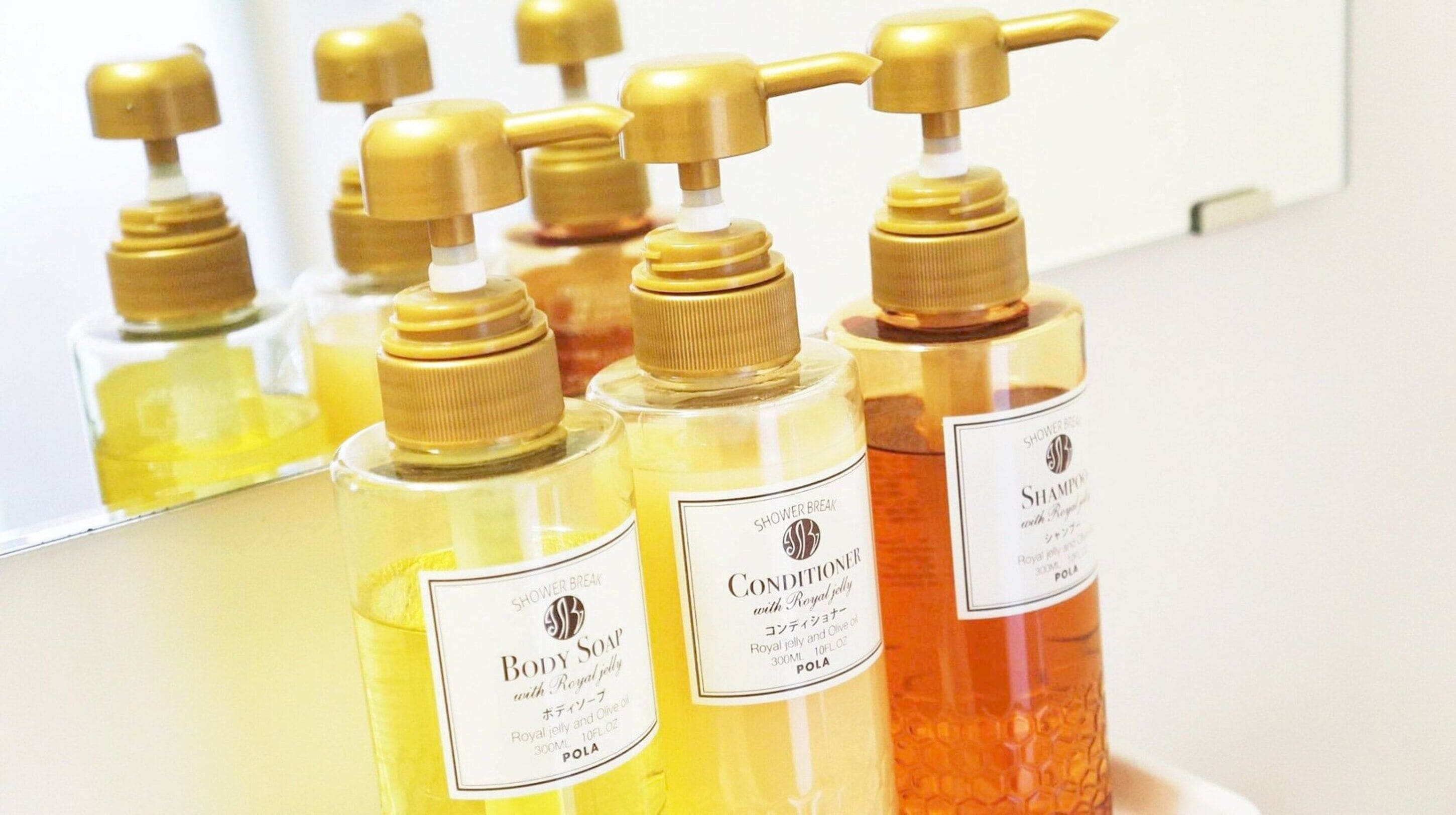 Bottles of body soap and conditioner with royal jelly and olive oil, displayed in a bathroom setting.