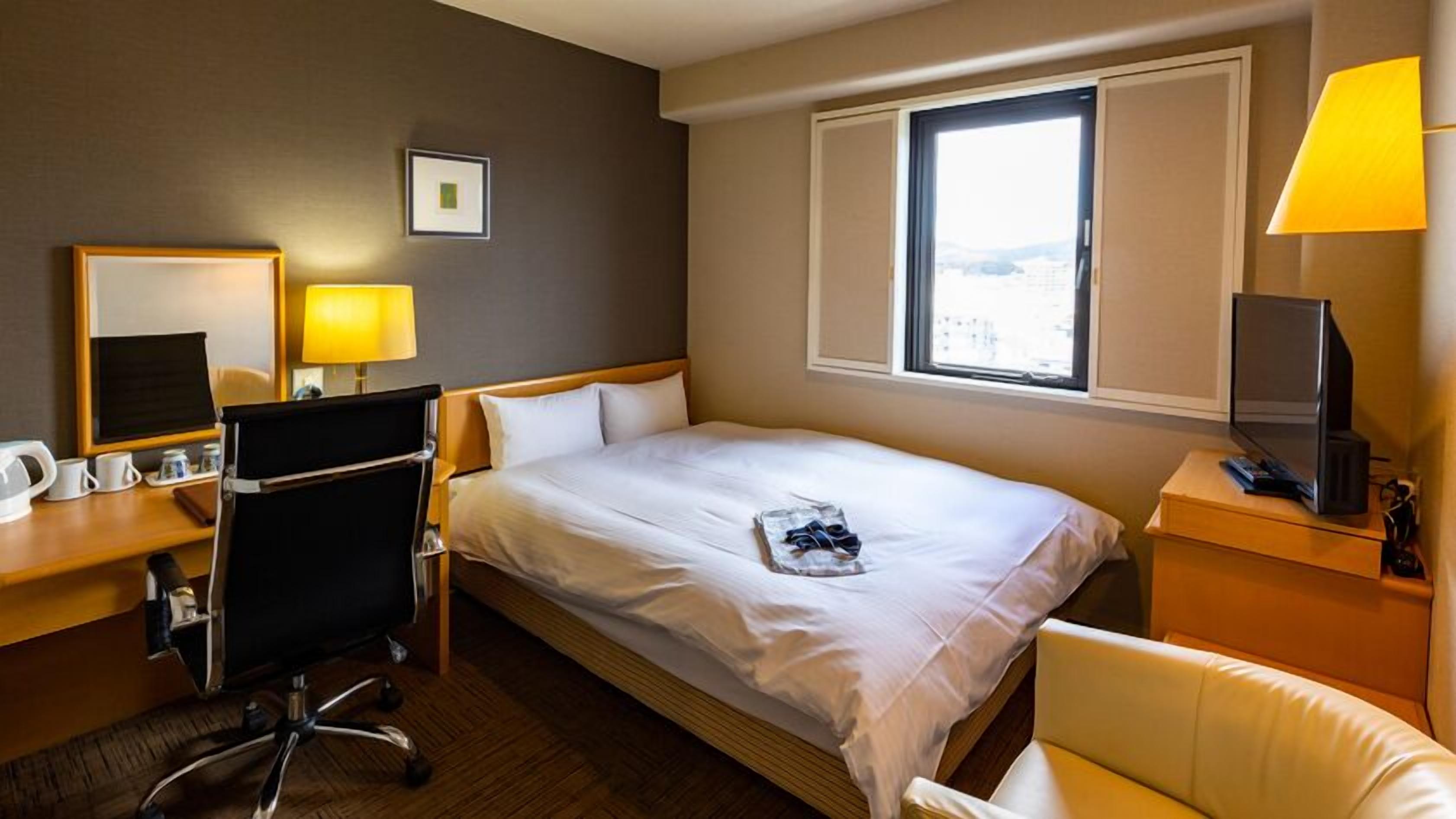 A hotel room with a bed, desk, chair, TV, and window.