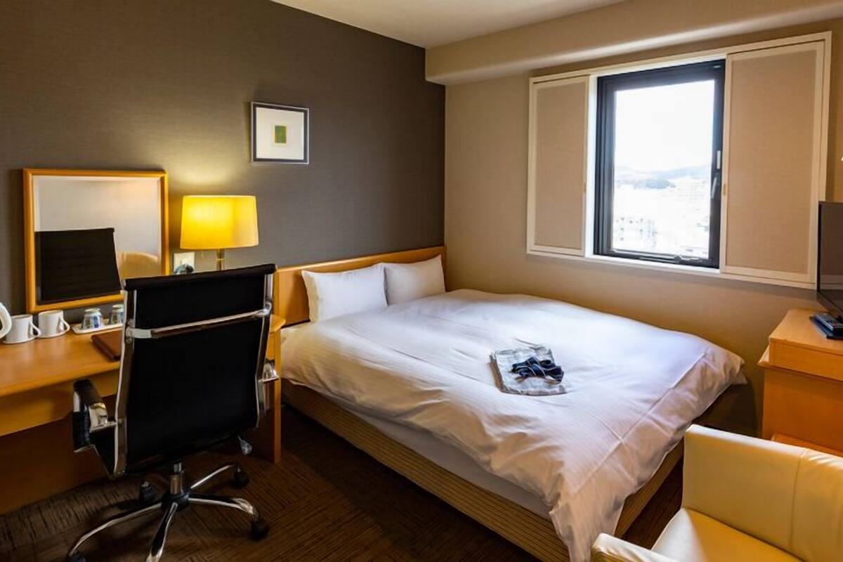 A hotel room with a bed, desk, chair, TV, and window.